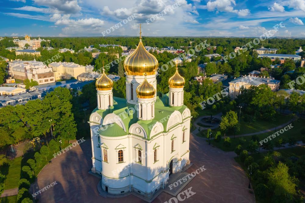 На фотографии изображен Екатерининский собор в Пушкине, который является одной из главных достопримечательностей Царского Села. Собор был построен в стиле русского зодчества и украшен пятью золотыми куполами, символизирующими православную веру. Окружённый зеленью парков, он создаёт атмосферу спокойствия и гармонии. Пушкин — это исторический пригород Санкт-Петербурга, известный своими дворцами и садами, а собор — духовное сердце этого места.